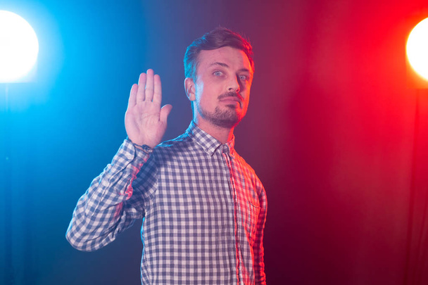 Ernstige jonge bebaarde knappe hipster man toont Palm up beelzende stop op blauw-rode achtergrond. Begrip afwijzing. - Foto, afbeelding