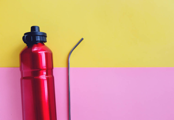 Flache Lage aus metallischem Edelstahl-Stroh und Mehrwegflasche für Getränke auf leuchtendem rosa und gelben Hintergrund, nachhaltiger Produktlebensstil und Null-Abfall-Konzept  - Foto, Bild