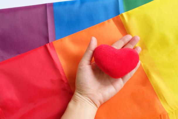 ręka trzyma kształt serca nad tęczy LGBT duma flaga z sercem na białym tle  - Zdjęcie, obraz