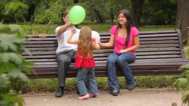 Family play game with balloons sitting on bench in park - Filmagem, Vídeo