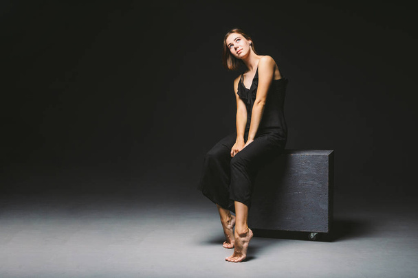 Jeune mannequin femme caucasienne posant en studio fond noir.Fille assise dans une robe noire sur un mur sombre. Sujet grave mauvais état psychologique, intra, problèmes, conflit de personnalité
 - Photo, image