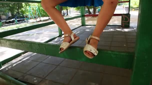 Little girl costs on handrail of gazebo among children's playground - Filmmaterial, Video