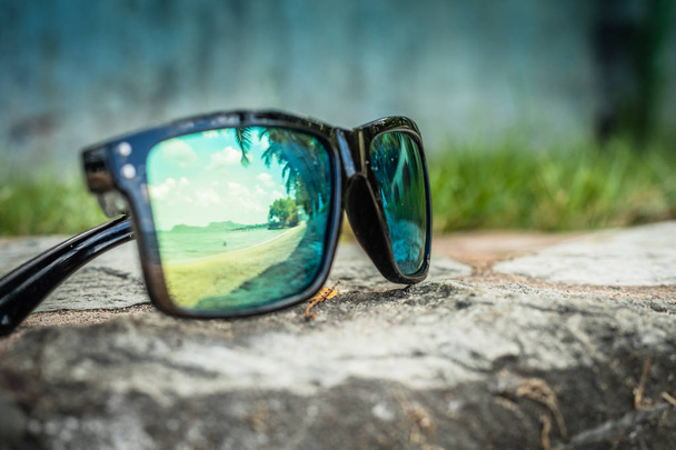 Fashionable sunglasses. Sunglasses with mirrored lenses. Reflection of the beach and tropical palm trees in sunglasses - Photo, Image