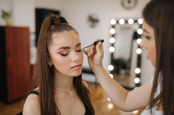 Visagistin macht professionelles Make-up für junge rothaarige Frau mit Sommersprossen - Foto, Bild
