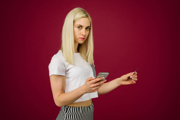 Eine junge Frau hält ein Smartphone und eine Kreditkarte in der Hand. Probleme mit einer Bankkarte, wegen Sperrung oder falsch eingegebener PIN. - Foto, Bild