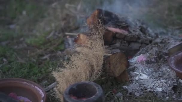 Smoldering steaming log and ash on the ground near clay bowls, stone mortar and pestle, indian grass, sorghastrum nutans - Footage, Video