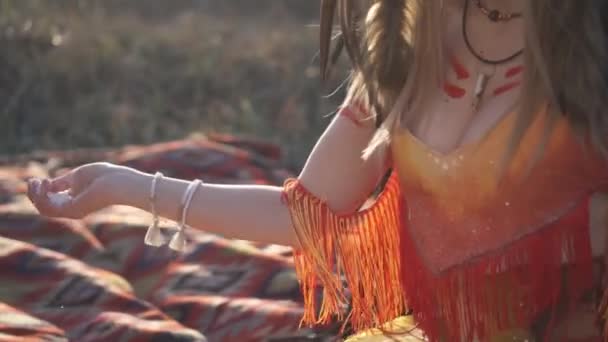 Beautiful girl in native american indian headdress and costume with colorful make-up hold powder in her hands. she claps her hands and the powder scatters in the wind - Footage, Video