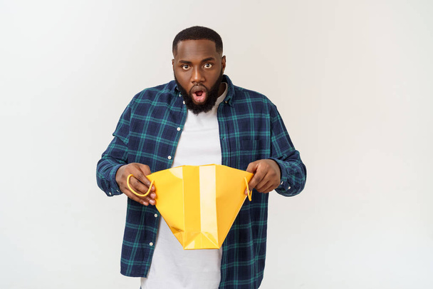 Young african american man surprised while holding a lot of shopping bags on grey background - Photo, Image