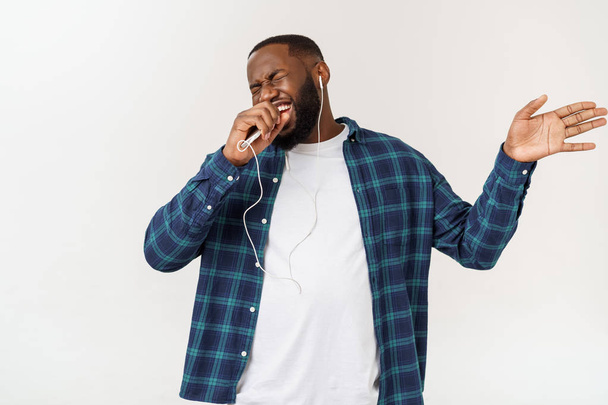 カジュアルな服を着たハンサムなアフロアメリカンの男性は、スマートフォンを使用して音楽を聴いて笑顔. - 写真・画像