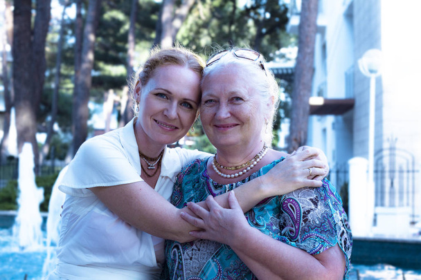 Senior woman and her daughter spending time together in the city park. elderly mom and daughter smile and hug happily. Close-up portrait of Mother With Adult Daughter In Park. Happy Mothers' Day - Foto, Imagen