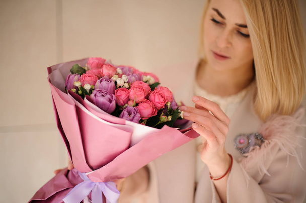 Girl in the coat looking at the bouquet of purple violet and pink flowers - Photo, Image