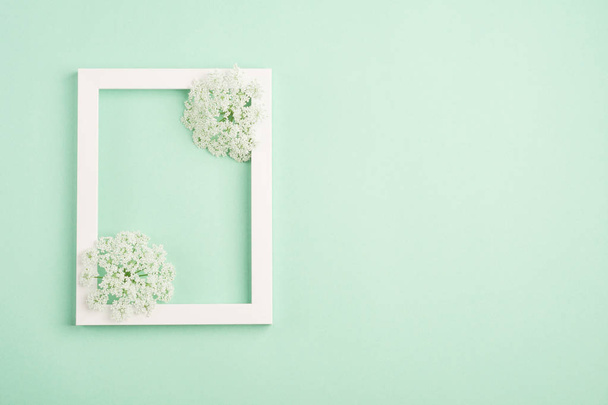 Hermosas flores blancas y marco en blanco sobre fondo de menta pastel. Color de luz suave. Vista superior, espacio de copia
. - Foto, Imagen