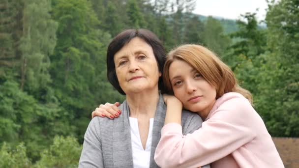 Portrait of a serious mother and adult daughter against the backdrop of the mountains in the summer. Happy old age, mothers day, daughter travels with an elderly mother - Footage, Video