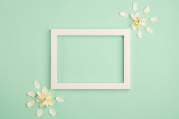 Flowers composition. Beautiful white flowers and blank frame on pastel mint background. Top view, copy space. - Foto, Imagem