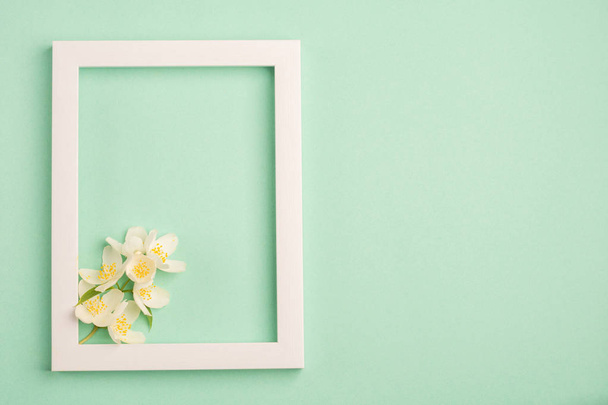Beautiful white flowers and blank frame on pastel mint background. Top view, copy space. - Фото, зображення