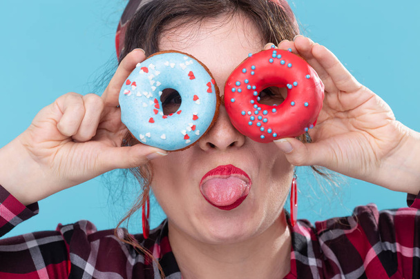 Dieta, deser i Junk Food-bliska pin-up ładna kobieta z pączkami pokazując język na niebieskim tle - Zdjęcie, obraz