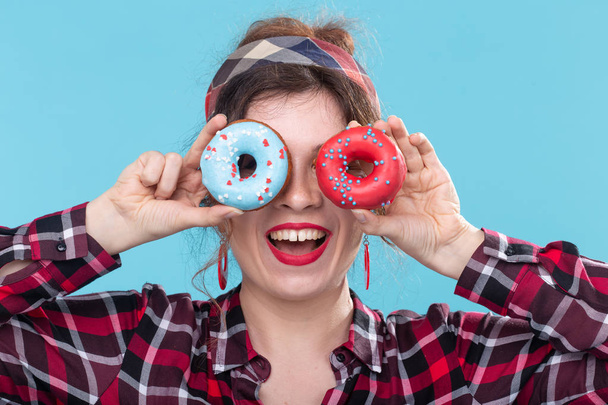 Diet, dessert and junk food - close up of pin-up pretty woman with doughnuts on blue background - Photo, Image