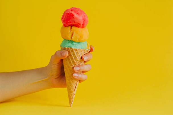 female hand holding waffle cone ice cream isolated on a vibrant yellow background, copy space - Fotó, kép