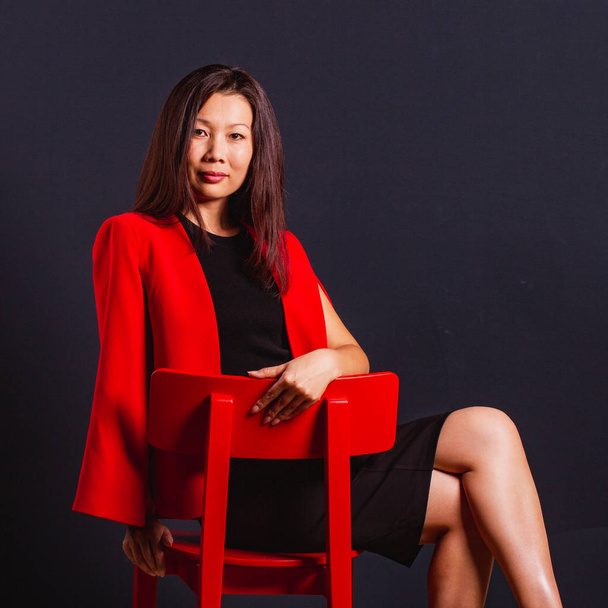 Gyönyörű ázsiai üzleti nő ül egy piros szék, és úgy néz ki  - Fotó, kép