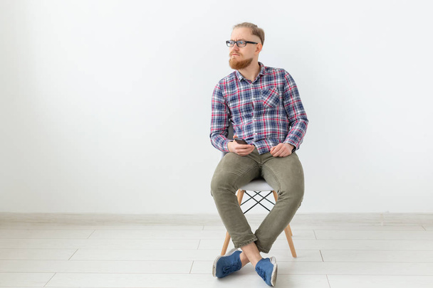 junger Mann mit Hipster-Bart sitzt über weißem Hintergrund mit Kopierraum - Foto, Bild