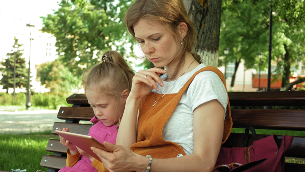 Mom and daughter use gadgets in the open air. Summer - Filmmaterial, Video