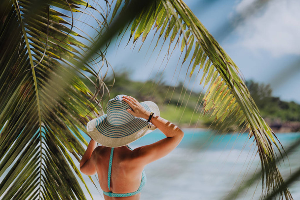 Woman on the beach in the palm trees shadow wearing blue hat. Luxury paradise recreation vacation concept - Photo, Image