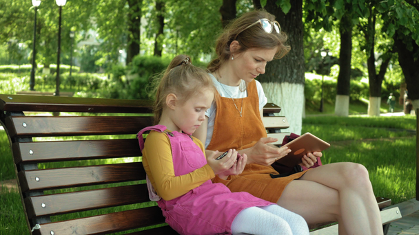 Mom and daughter use gadgets in the open air. Summer - Filmmaterial, Video