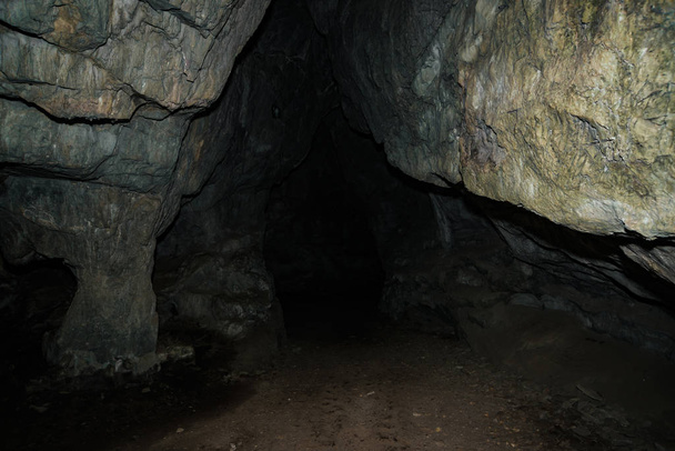 Nádherná jeskyně. Pohled z vnitřní temné kobky. Stěny jeskyně s texturou. Obraz podzemního tunelu. Vlhkost uvnitř jeskyně. Světlo na konci tunelu. - Fotografie, Obrázek