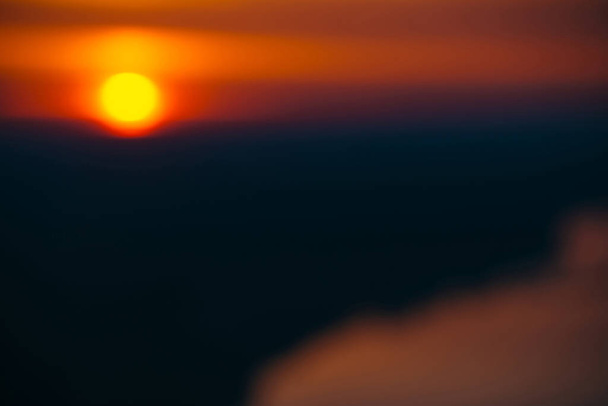 Blurry background image of circle of sun rising from behind dark horizon on background varicolored clouds of warmly shades above river. Abstract picturesque image of sun in bokeh. - Photo, Image
