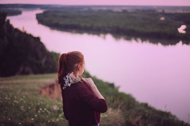 The girl is standing with her back in the field against the background of the river, nature.  - Photo, Image
