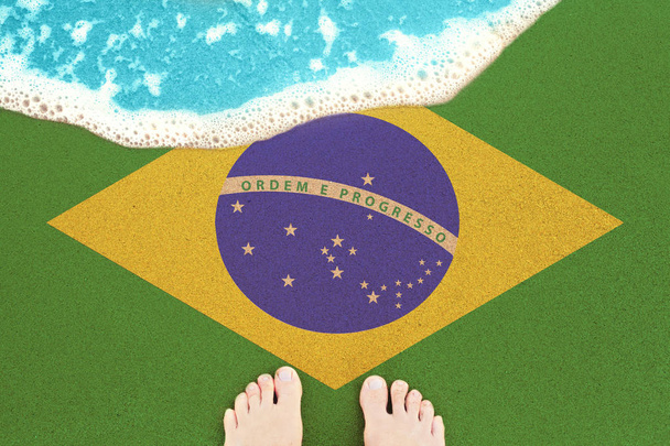 Πόδια στην αμμώδη παραλία με σημαία Βραζιλίας. Θέα από πάνω στο σέρφινγκ. - Φωτογραφία, εικόνα