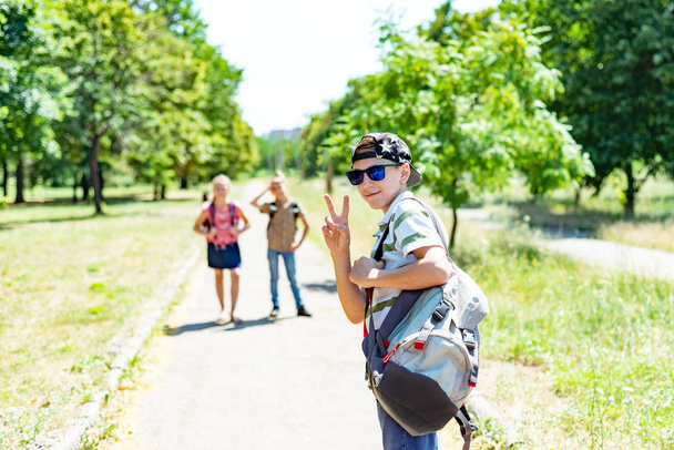 Un mec élégant avec une casquette et des lunettes de soleil et un sac à dos avec des amis va étudier. Les enfants vont à l'école
. - Photo, image