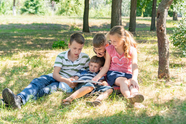 Kinder lernen in der Natur, vier Kinder lesen im Park unter freiem Himmel ein Buch. Schüler bereiten sich auf die Schule vor. - Foto, Bild