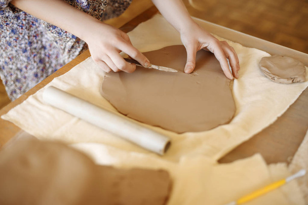 female hands make a plate of clay - Foto, afbeelding