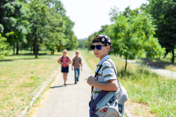 Stylish guy in a cap and sunglasses and a backpack with friends goes to study. Children go to school. - Photo, Image