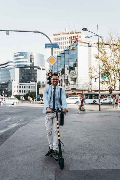 Young modern man using and driving electric scooter on city street. Modern and ecological transportation concept. - Foto, Imagen
