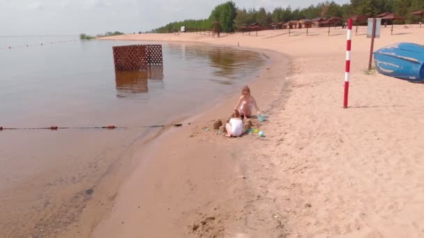 Mamá e hija están jugando en la playa, construyendo un castillo de arena. Día soleado de verano. vacaciones. Disparo aéreo
  - Metraje, vídeo