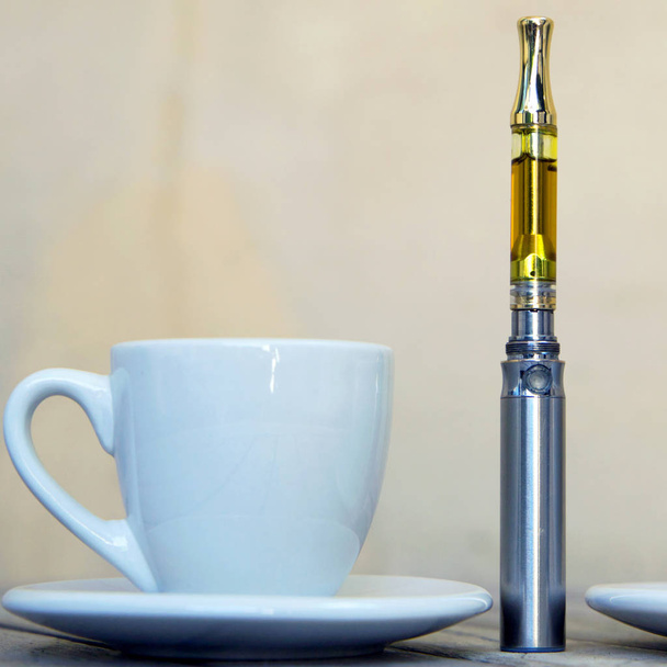 Vape Pen und Tasse auf Holzoberfläche, Marihuana-Öl verdampfend, Cannabis-Vaporizer  - Foto, Bild