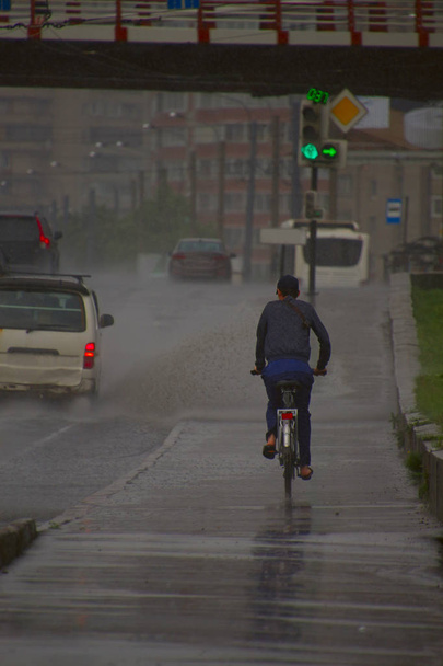 車からのスプレーで雨の中で自転車に乗っている男 - 写真・画像
