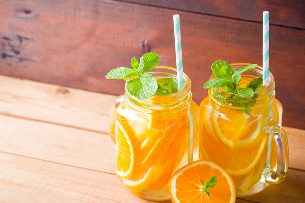 Fruit infused water with orange, lemon and mint. Mug delicious refreshing drink of mix fruits with mint on wooden boards. Iced summer drink in mason jar. Fresh homemade lemonade - Фото, зображення
