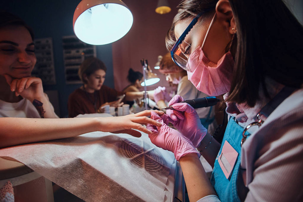 Focused diligent manicurist is working at her workplace at manicure salon - Fotó, kép