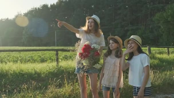 Three girls children with bouquet of flowers show finger on the road, emotions joy and happiness, wait and meet - Imágenes, Vídeo