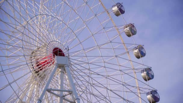 Великий фрагмент обертового білого гіганта колеса Ферріса з круглими закритими кабінами в парку розваг катається на тлі блакитного неба з хмарою в теплий літній вечір. Частина великої каруселі на ярмарку
 - Кадри, відео