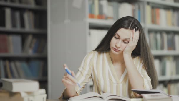 Κουρασμένη μελαχρινή γυναίκα ετοιμάζεται για εξετάσεις στη βιβλιοθήκη του πανεπιστημίου - Πλάνα, βίντεο