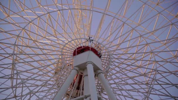 Fragmento de rueda gigante blanca giratoria Ferris con cabinas redondas cerradas en paseo por el parque de atracciones en el fondo del cielo azul en la cálida noche de verano al atardecer. Parte del gran carrusel en la feria de vacaciones
. - Imágenes, Vídeo