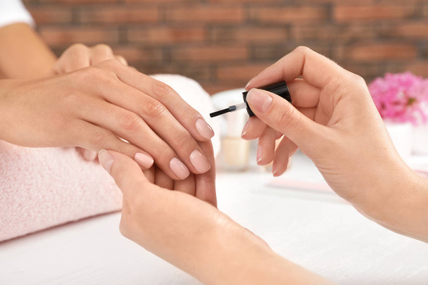 Manicurist toepassen van Poolse op de nagels van de klant aan tafel, close-up. Spabehandeling - Foto, afbeelding