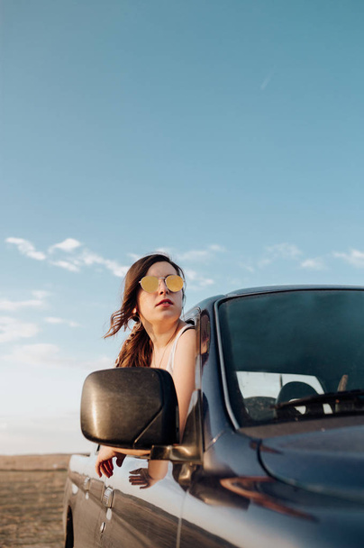 Güneş gözlüklü genç gezgin kadın 4x4 arabasıyla gün batımında gezintiye çıkıyor. - Fotoğraf, Görsel