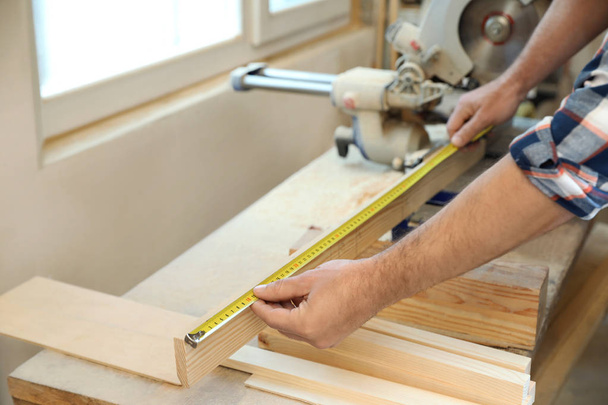 Working man measuring timber strip in carpentry shop, closeup - Foto, afbeelding