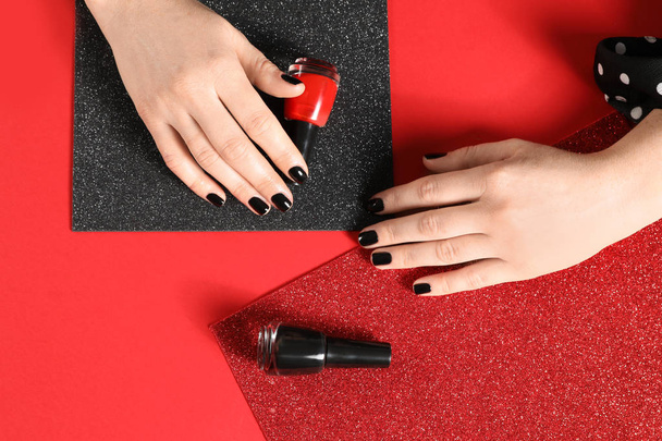 Woman with black manicure and nail polish bottles on color background, top view - Foto, afbeelding