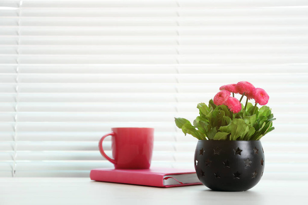 Window with blinds, beautiful potted plant, notebook and cup on sill, space for text - Фото, изображение